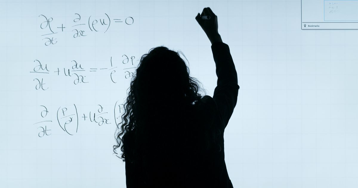 STEM woman stood at a board writing and solving partial differential equations for engineering.